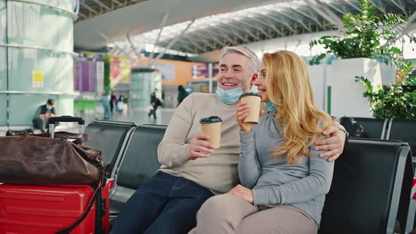 Happy Middle Aged Couple Enjoying Takeaway Coffee Waiting for Flight Together Sitting at Airport