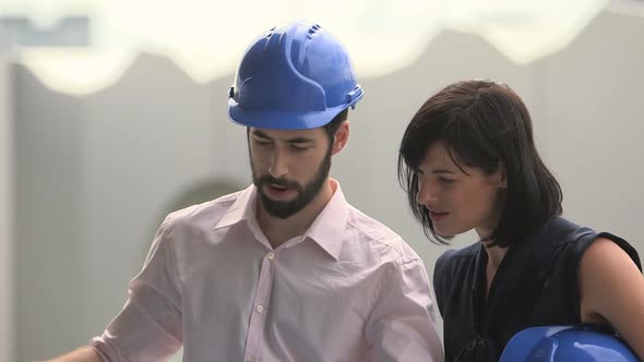 Man and woman discussing with blueprint at construction site