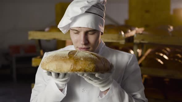 Close View of Baker in Uniform Sniffs Fresh Loaf of Bread and Has Pleasure