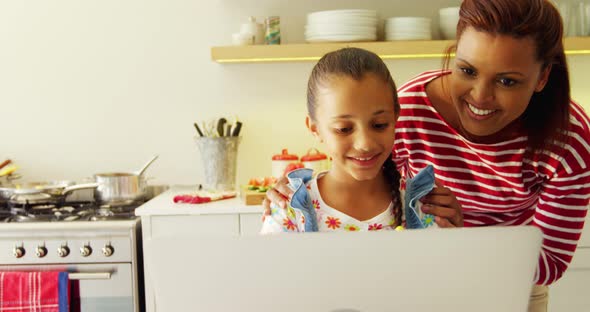 Mother and daughter using laptop in kitchen worktop 4k