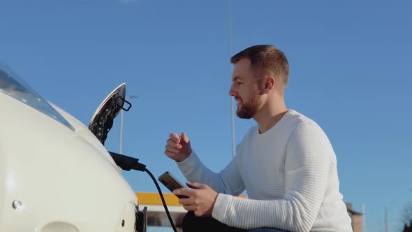 A Fairskinned Male Driver Connects an Electric Car to the Power System to Charge the Car Battery and