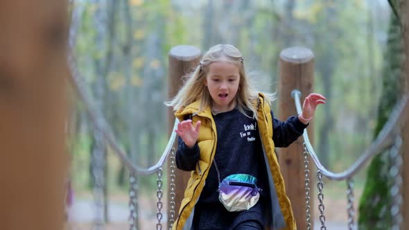 Funny Little Girl Running Towards the Camera Over a Rope Bridge in the Park