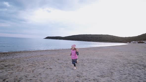 Cute little girl in pink hat runs along the beach along the sea in spring time. Freedom concept