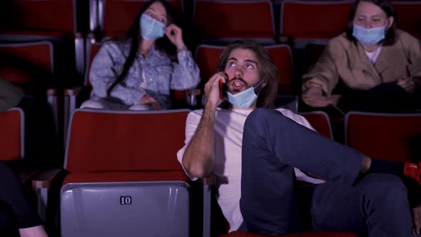 Confident young man talking on mobile phone in cinema, spectators looking angry