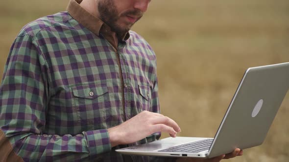 Handheld Farmer Man Stands in the Field of Rye and Works on a Laptop Investigating Plants Ecologist