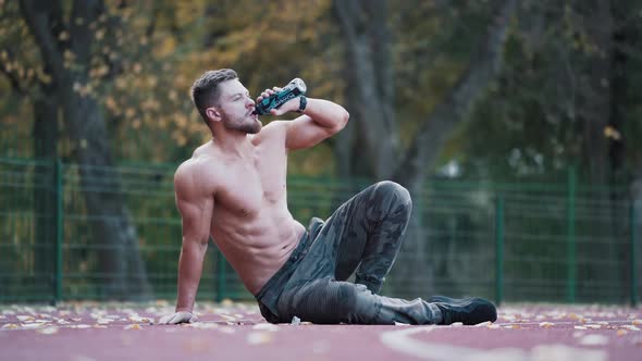 Handsome athlete drinks water outdoors. 