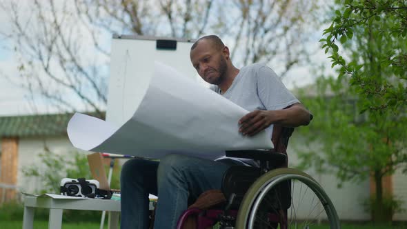 Serious Smart Skilled Architect in Wheelchair Looking at Blueprint Shaking Head