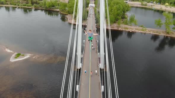 The Man Sits in a Lotus Position on a Rope Stretched Between the Supports of the Bridge at High