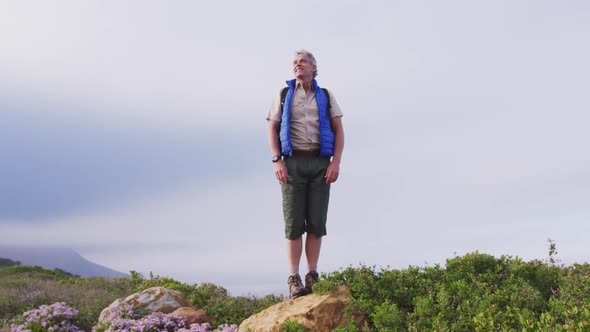 Senior hiker man standing with his arms wide open standing on a rock while trekking in the mountains