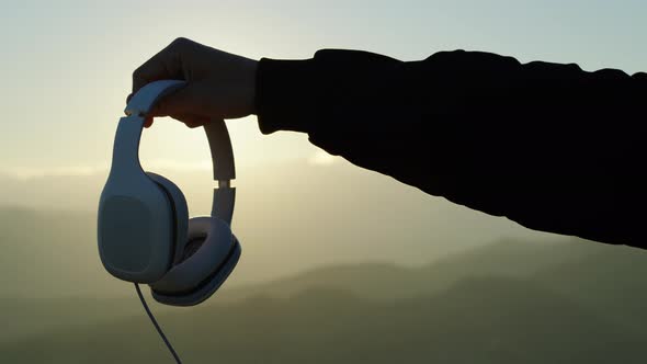 Hand holds music headphones in silhouette