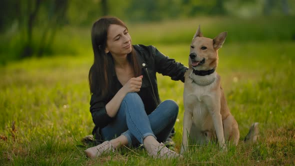 Female, Sitting on the Groung in Park, Stroking Her Dog.