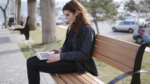 Attractive Female in Her 20's Wearing Hipster Urban Outfit Sitting on the Bench and Typing Something