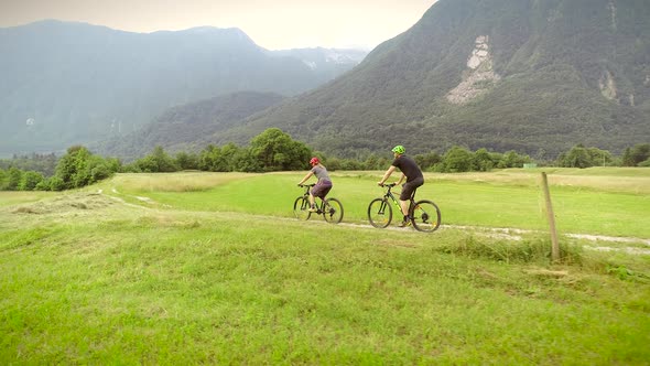 Aerial view of a couple driving mountain bikes on dirt road surrounded by hills.