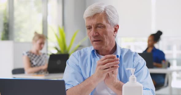 Mature Businessman Washing Hands with Antiseptic Gel Before Working on Computer in Office
