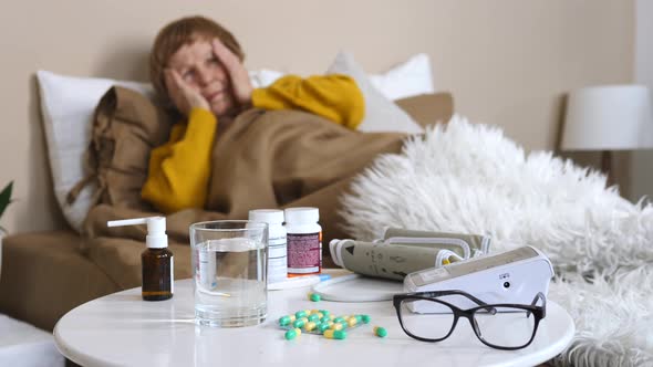 Sick Old Woman Lying In Bed With Medicine And Glass Of Water On Table