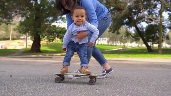 Little Boy Standing on Skateboard, Rolling with Help of Mother 
