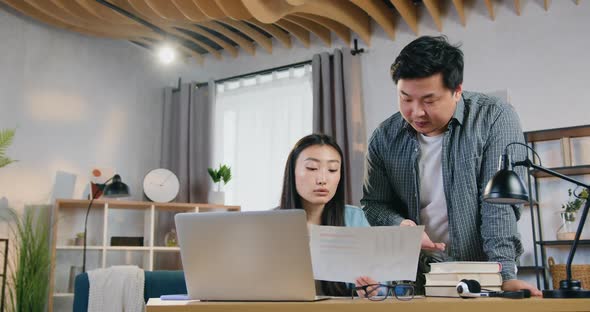 Asian Father Standing Near His Daughter and Helping with University Hometask on Computer