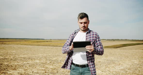 Farmer with Digital Tablet Checking on Field of Grain Sorghum