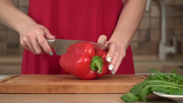 A Woman in the Kitchen Cuts a Red Paprika with a Knife in the Kitchen