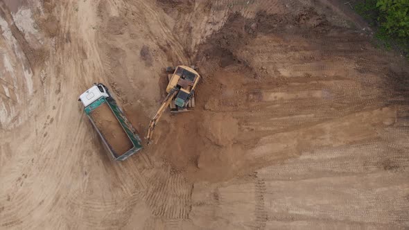 Aerial top view: yellow excavator pouring soil into tipper.