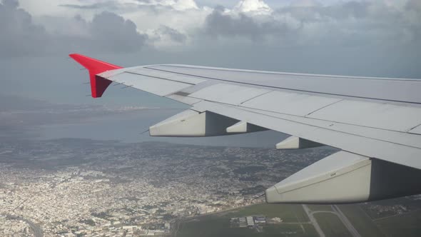 The Plane Flies Over the City in Gray Clouds, View From the Airplane Window To the Wing