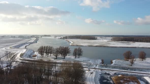 Flying towards a river with a drone above a frozen ditch in a winter landscape.