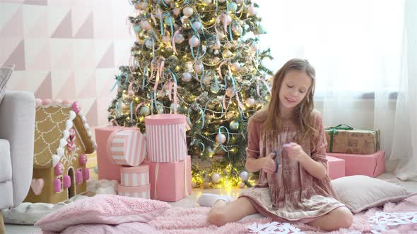 Adorable Little Girl Sitting Near the Tree and Making Paper Snowflakes