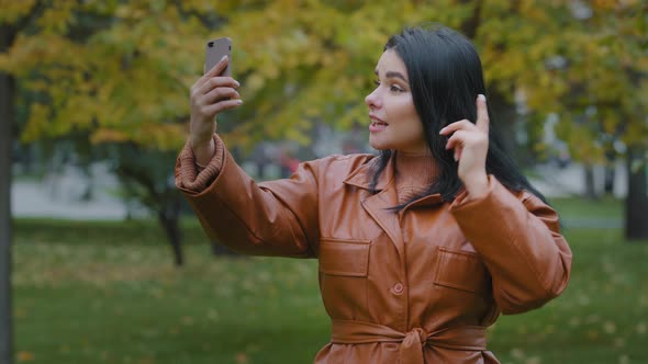Hispanic Woman Standing Outdoors Looking at Screen Talking on Phone Using Video Call Share