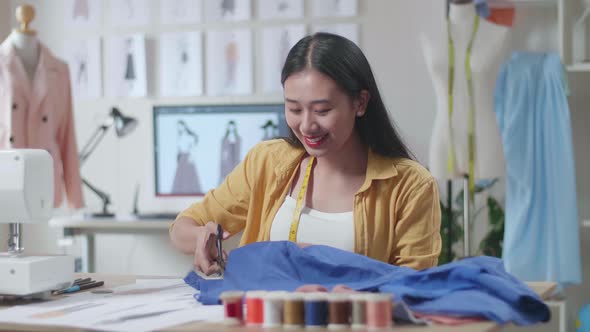 Female Designer With Sewing Machine Cutting Fabric With Scissor While Working On The New Dress