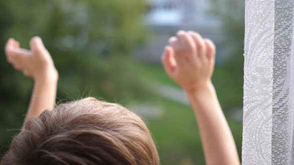 The Child Stands at the Window and Waving His Hands