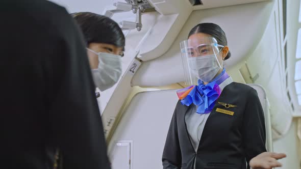 Asian flight attendants wearing face mask greeting passengers coming on board in airplane.