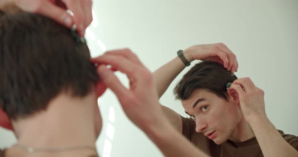 a Young Man Puts on a Cochlear Implant a Hearing Aid Looking at Himself in the Mirror