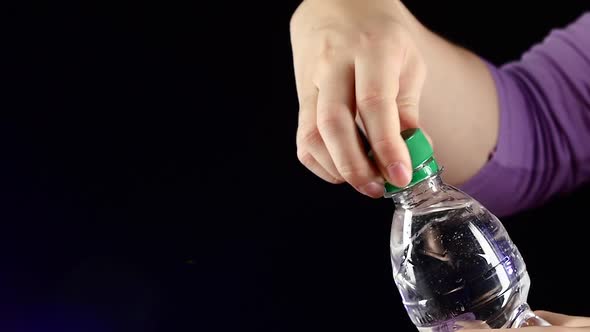 Hands Up and Opening a Green Bottle of Fresh Water on Dark, Slow Motion, Splash, Spray, Bubbles