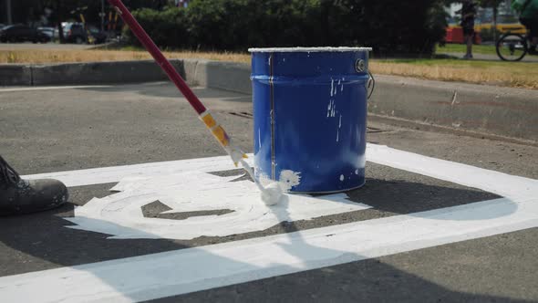 Male Worker Painting White Marking Line of Disabled Parking Lot Sign on Asphalt