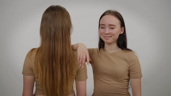 Charming Slim Young Woman Looking at Camera Smiling Holding Hand on Shoulder of Twin Sister Back