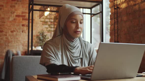 Muslim Businesswoman in Hijab Using Laptop and Posing for Camera in Cafe
