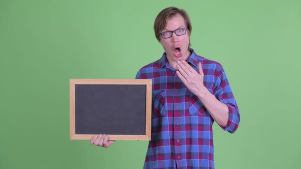 Young Hipster Man Holding Blackboard and Looking Shocked