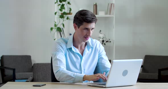 Attractive Caucasian Man Sitting with Laptop Typing Smiles at Camera Showing Hand OK Sign