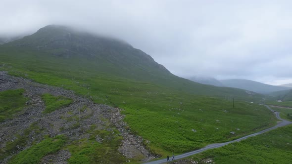 Two people walk down country round under mountain range