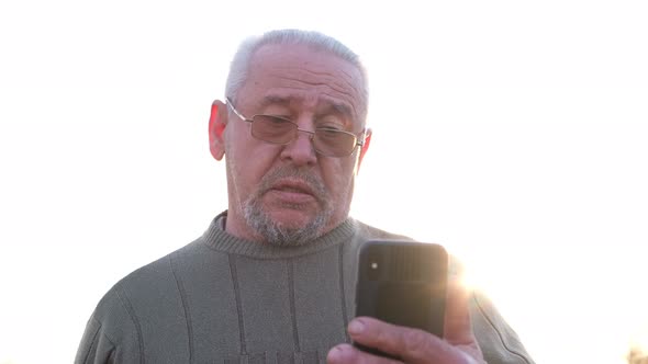 Mature Old Grayhaired Grandfather with a Smartphone in His Hands