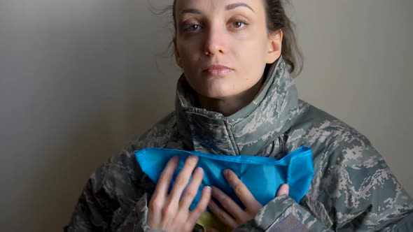 Young Female Soldier is Holding Ukrainian Flag with Love and Anxiety Due to Escalation Military