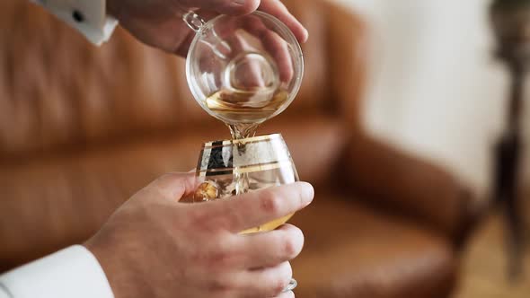 Closeup Male Caucasian Hands Pouring Drink From a Cup Into Cognac Glass