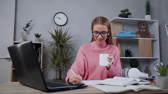 Girl in Pink Sweater which Sitting at the Table, Writing in the Notebook