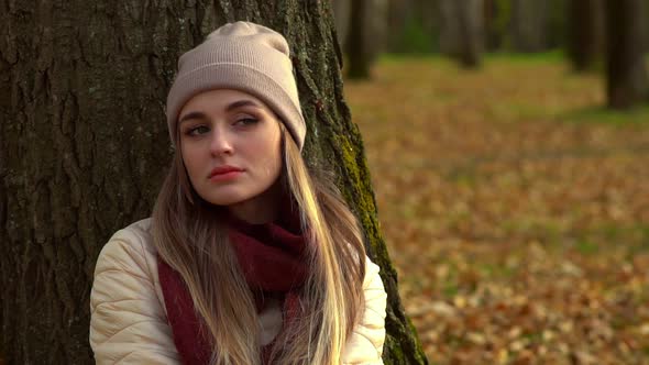 The Girl Sits Alone in the Autumn Park, on the Ground Under a Tree.