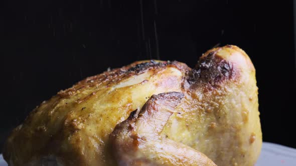 Baked crispy whole chicken revolving on black background.