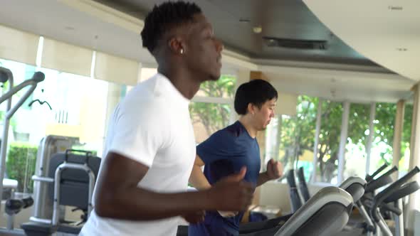 Multiethnic Asian and African American Males Running on Treadmills at Gym Club During Daytime