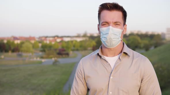 A Young Caucasian Man in a Face Mask Talks to the Camera on a Town's Outskirts