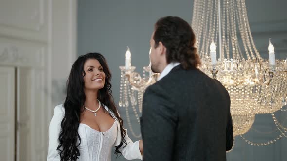 a Bride with Long Dark Hair and Big Breasts Touches the Pendants of a Crystal Chandelier and