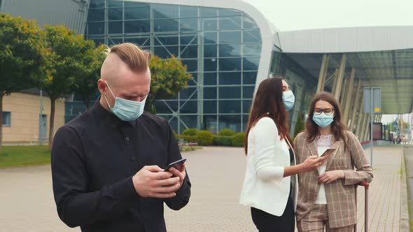 A Male Businessman and Two Girls in Medical Masks with a Mobile Phone Browse the Contents of the