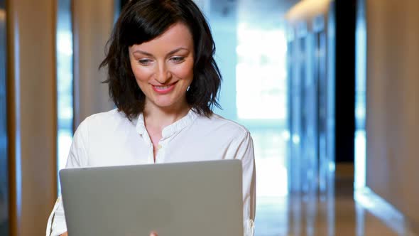 Female executive using laptop in corridor